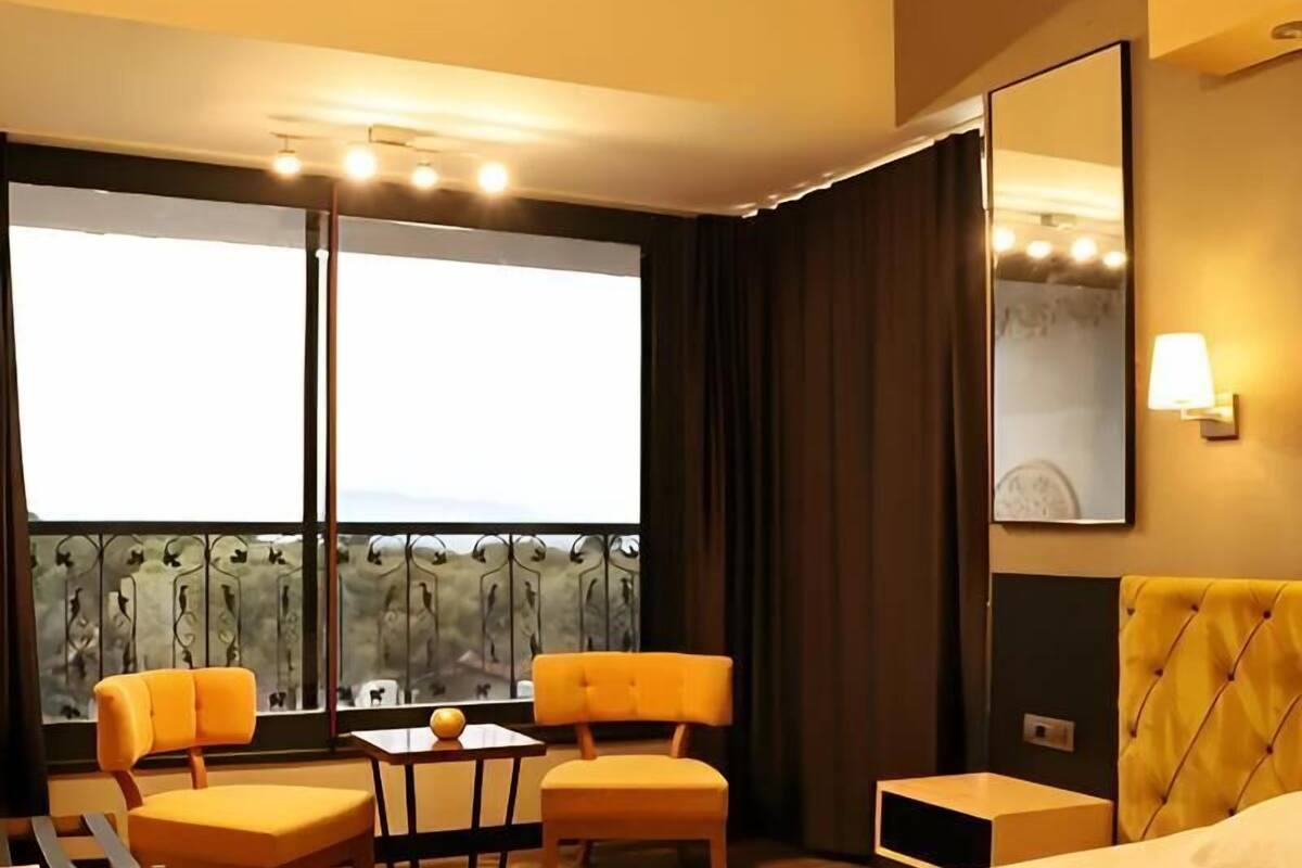 Een hotelkamer met een bed, een bureau, twee stoelen, een tafel, een balkon met uitzicht en een grote spiegel.