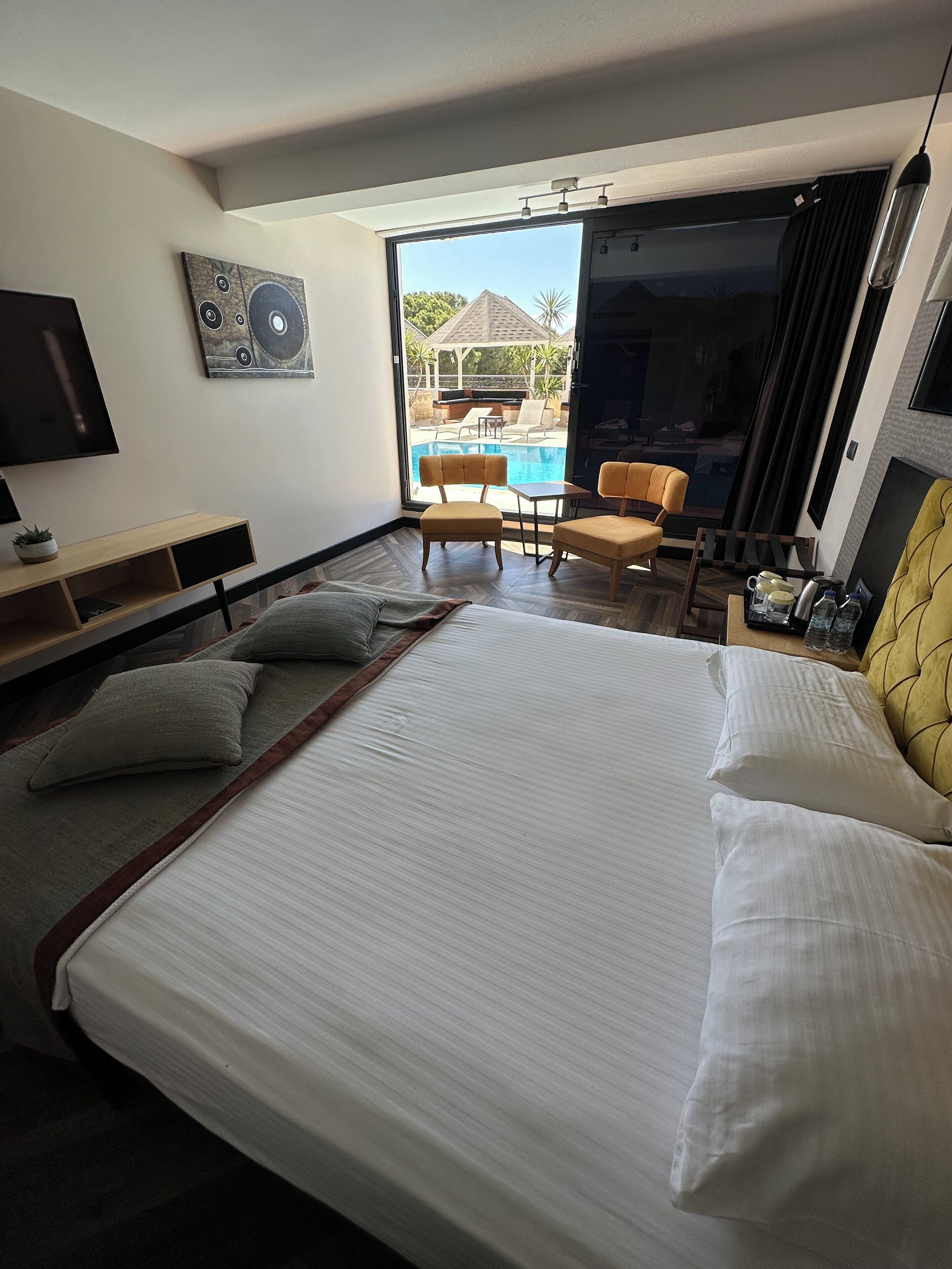 Une chambre d’hôtel avec un grand lit, une télévision, un bureau, une chaise et une vue sur une piscine extérieure.