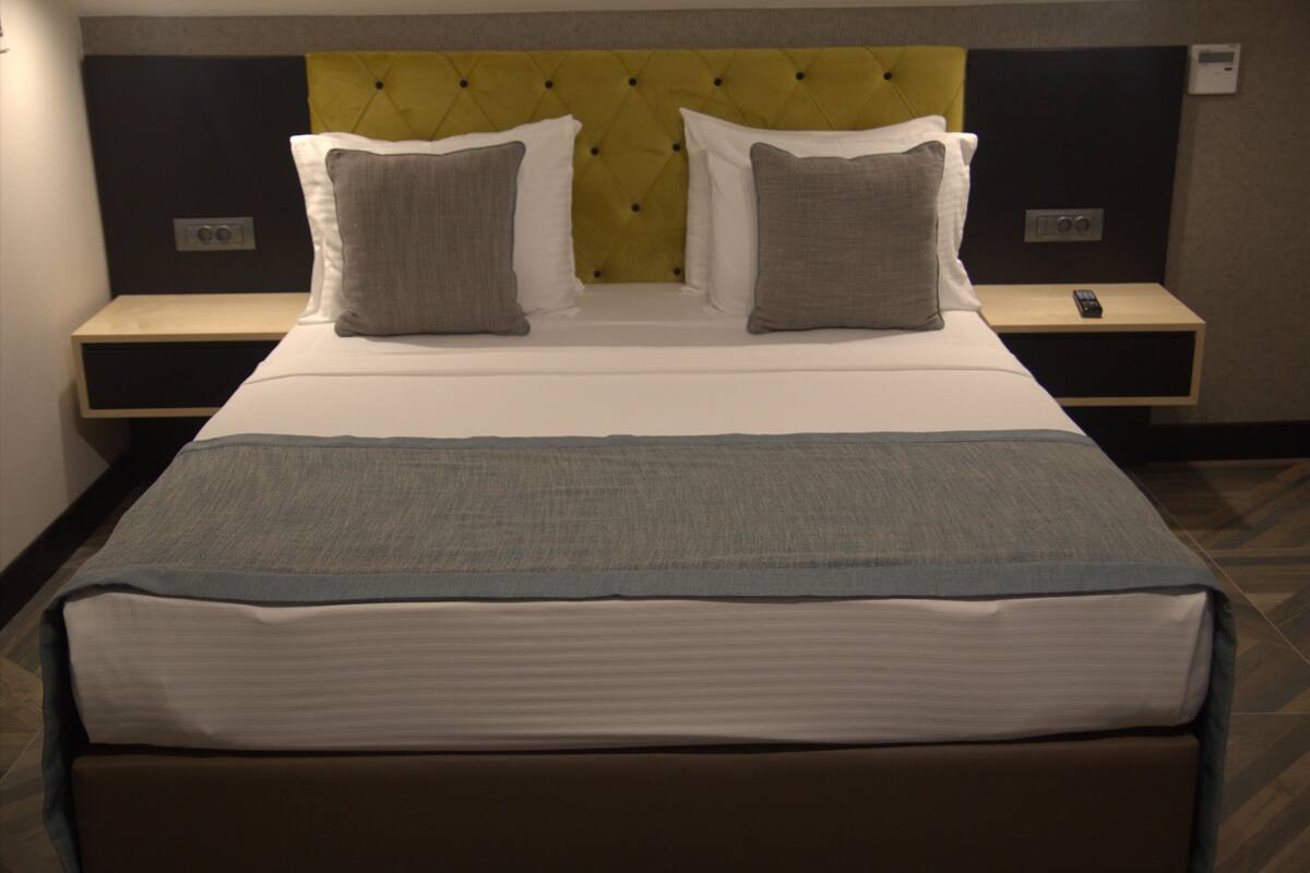 Een netjes opgemaakt bed met een hoofdeinde, twee nachtkastjes en een afstandsbediening op één van de nachtkastjes.