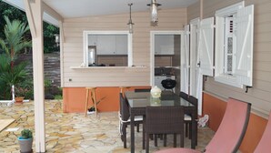 A covered patio with a stone floor, a dining table with chairs, a bar area, and a kitchen visible through an open door. - "Pied à terre to visit the north caribbean" (Le Carbet)