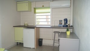 A compact kitchen with a refrigerator, a sink, a window with blinds, and a small bar stool. - "Pied à terre to visit the north caribbean" (Le Carbet)