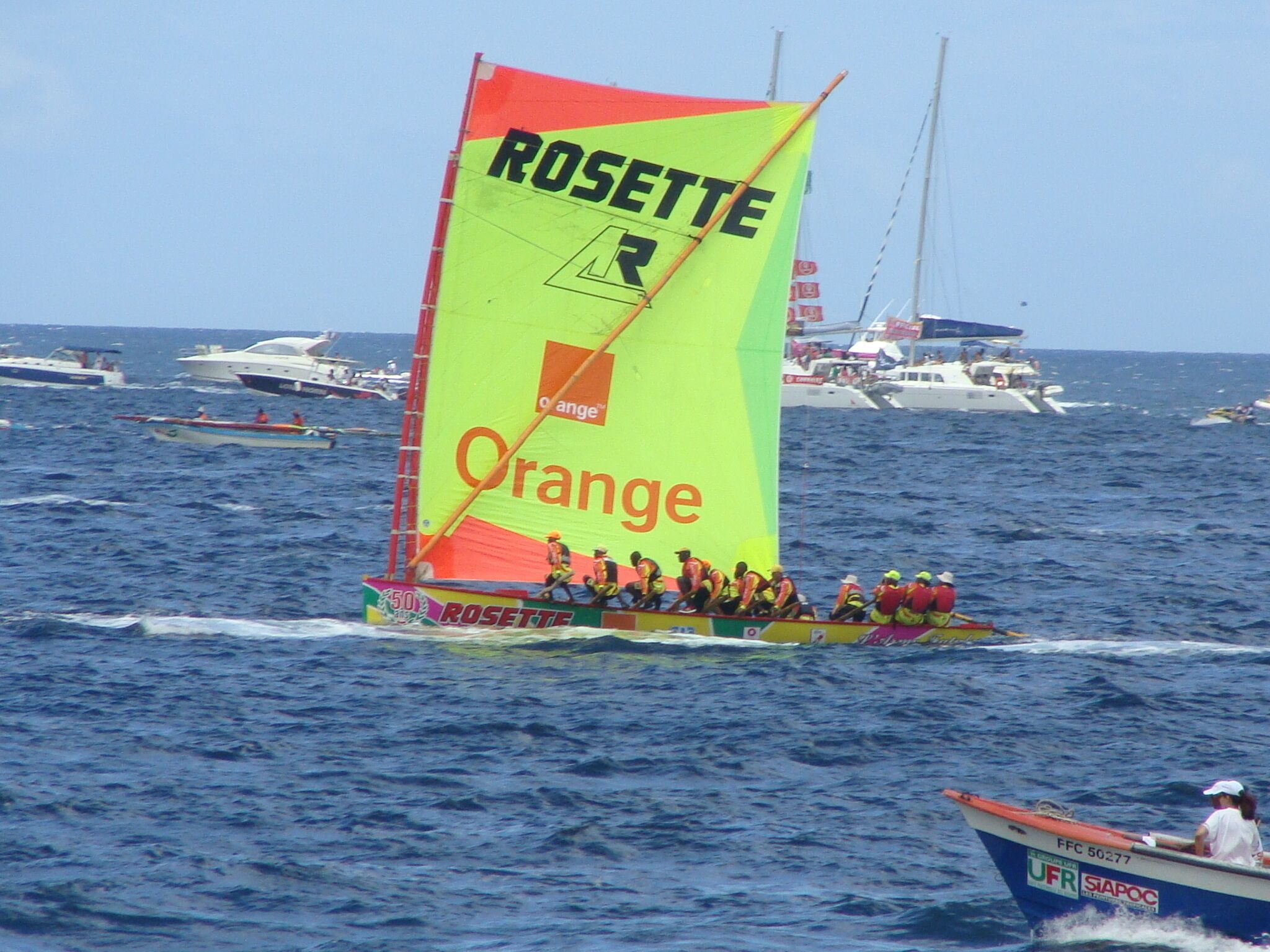 A sailboat with a large orange and yellow sail, named 'ROSETTE', on the water.