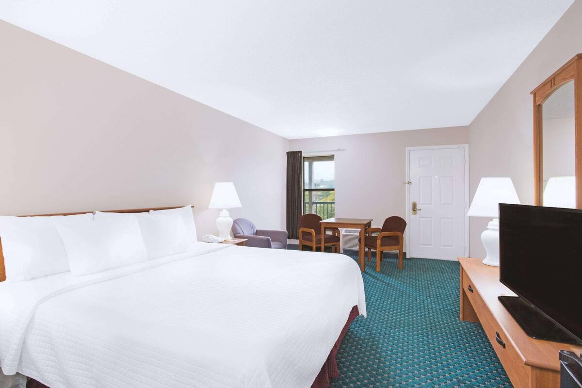 A hotel room with a bed, a desk, a chair, a television, and a door.