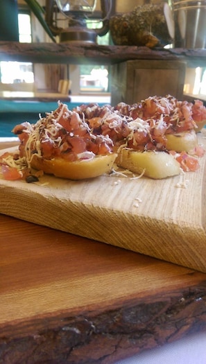 Una tabla de madera con pan en rodajas cubierto con una cobertura a base de tomate y queso rallado.