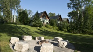 Een lodge met een vuurkorf van steen, omringd door grote rotsen, met op de achtergrond hoge bomen en een heldere lucht.