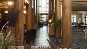 Een ruime lobby met hoge houten zuilen, een centraal geplaatste open haard van baksteen en een grote gewei-sculptuur.