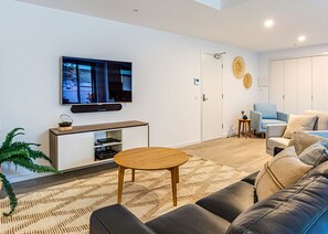 A modern living room with a flat-screen TV, a wooden coffee table, a sofa, and a small side table.