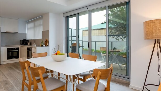 A modern kitchen with white cabinetry, a dining area with a white table and wooden chairs, and a large sliding glass door leading to an outdoor patio.