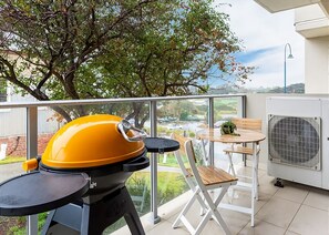 A balcony with a barbecue grill, a folding table, a chair, and a potted plant.