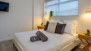 A modern bedroom with a large bed, bedside tables, a TV, and a window with a view.