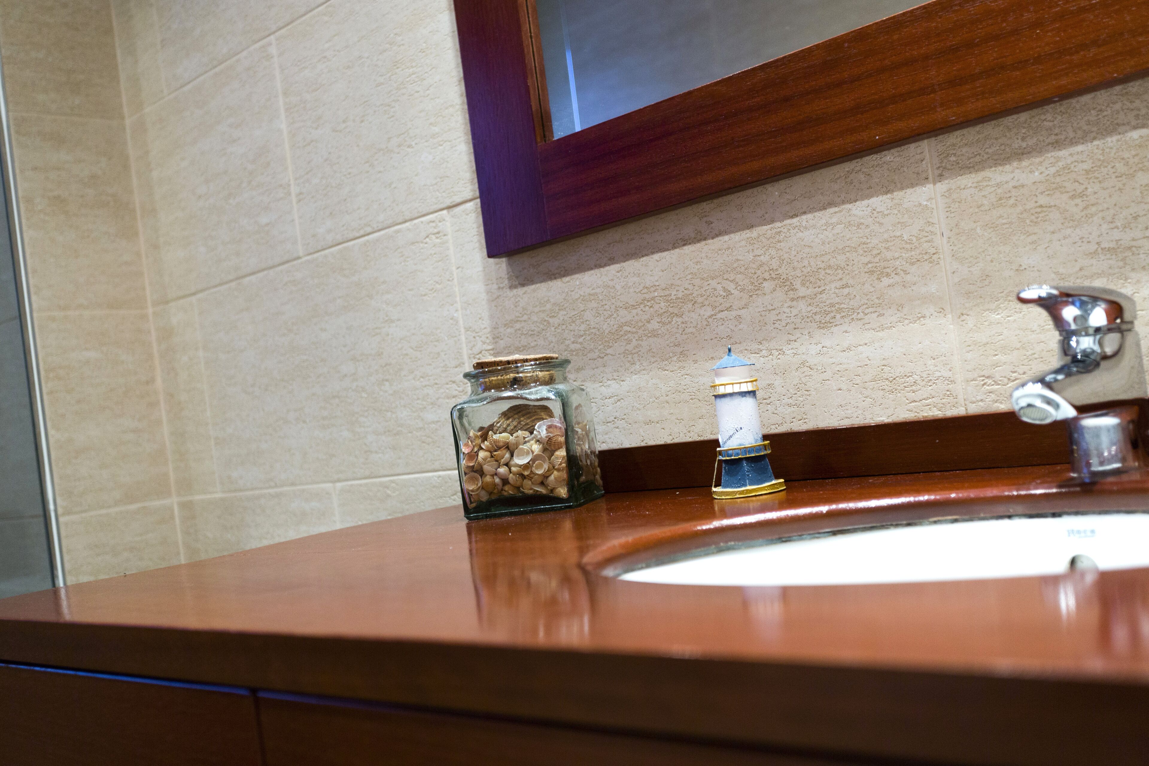 A bathroom sink with a wooden countertop, a glass jar with coins, and a soap dispenser.