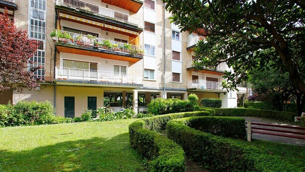 Ein mehrstöckiges Wohnhaus mit Balkonen, ein gepflegter Garten mit Hecken und ein gepflasterter Weg.