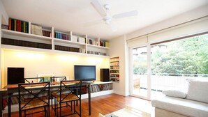 Ein modernes Wohnzimmer mit Holzboden, einem weißen Sofa, einem Couchtisch, einem Fernseher, einem Bücherregal und einem Deckenventilator.