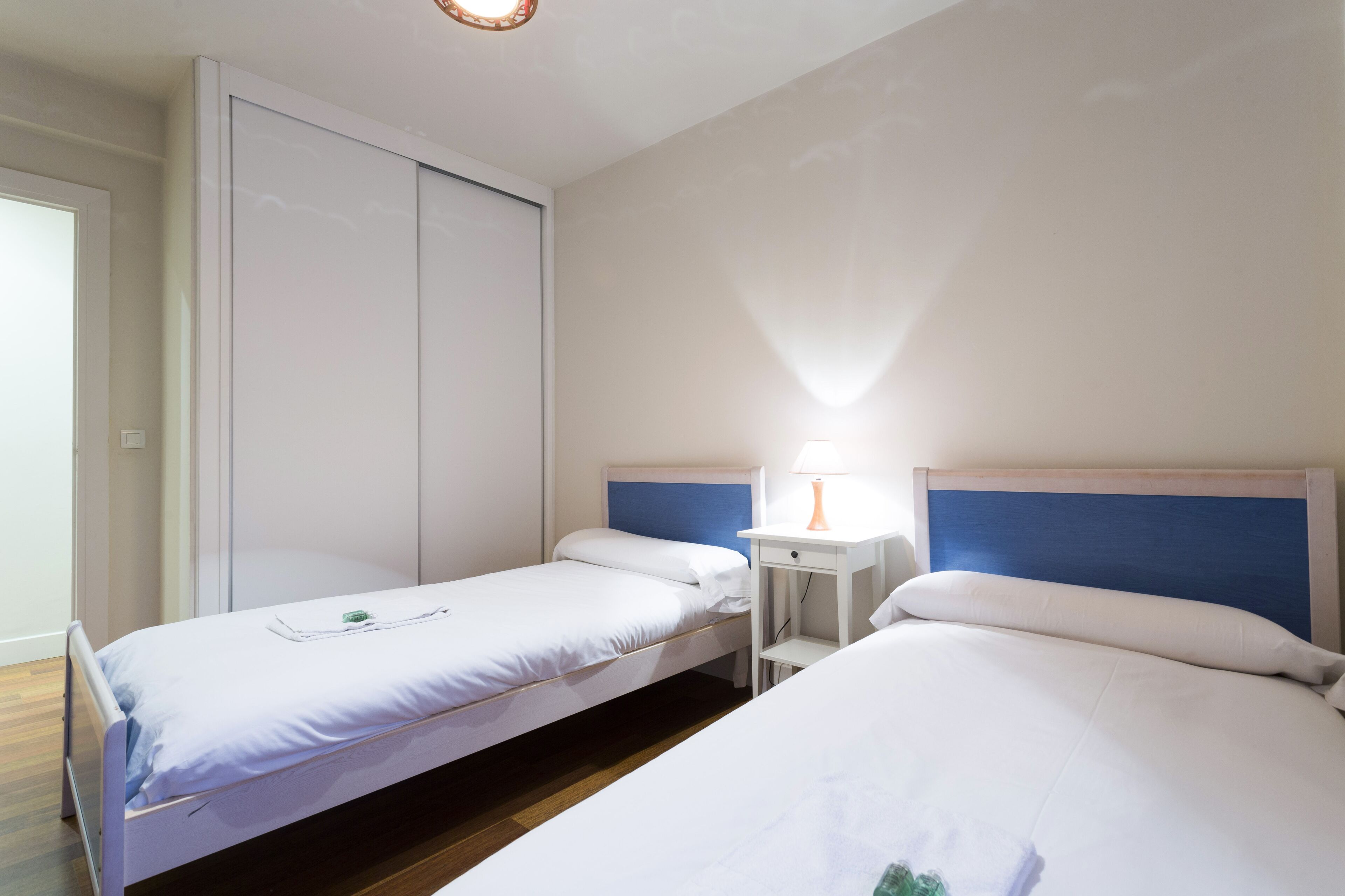 Une chambre d’hôtel avec deux lits simples, une table de chevet avec une lampe et une armoire.