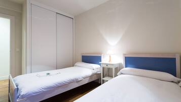 Une chambre d’hôtel avec deux lits simples, une table de chevet avec une lampe et une armoire.