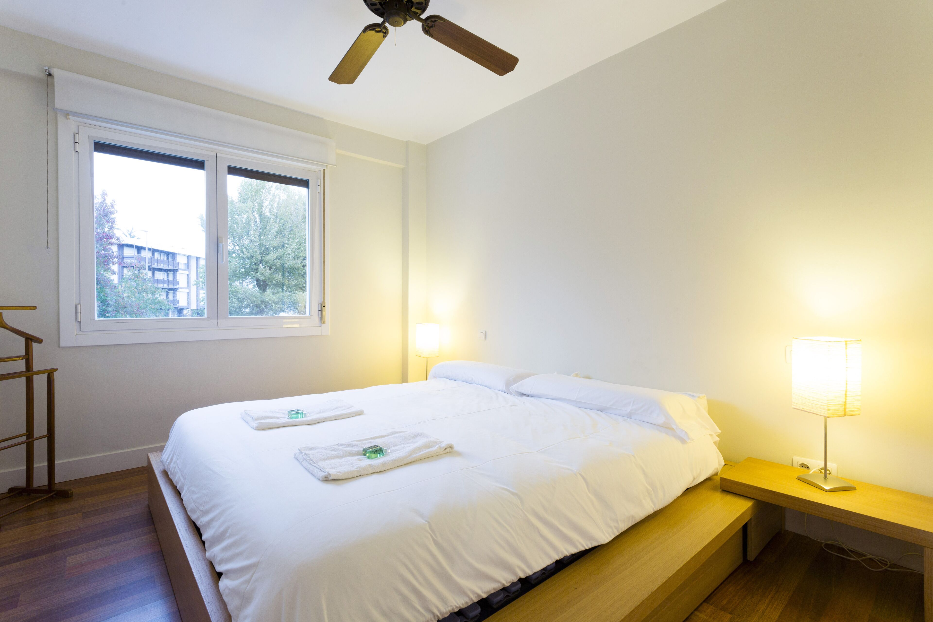 Une chambre à coucher avec un lit, des lampes de chevet, un ventilateur de plafond et une fenêtre.