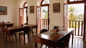 A dining area with a large wooden table, several chairs, and a view through open doors to the outside. - Pousada Convento da Conceição (Olinda)