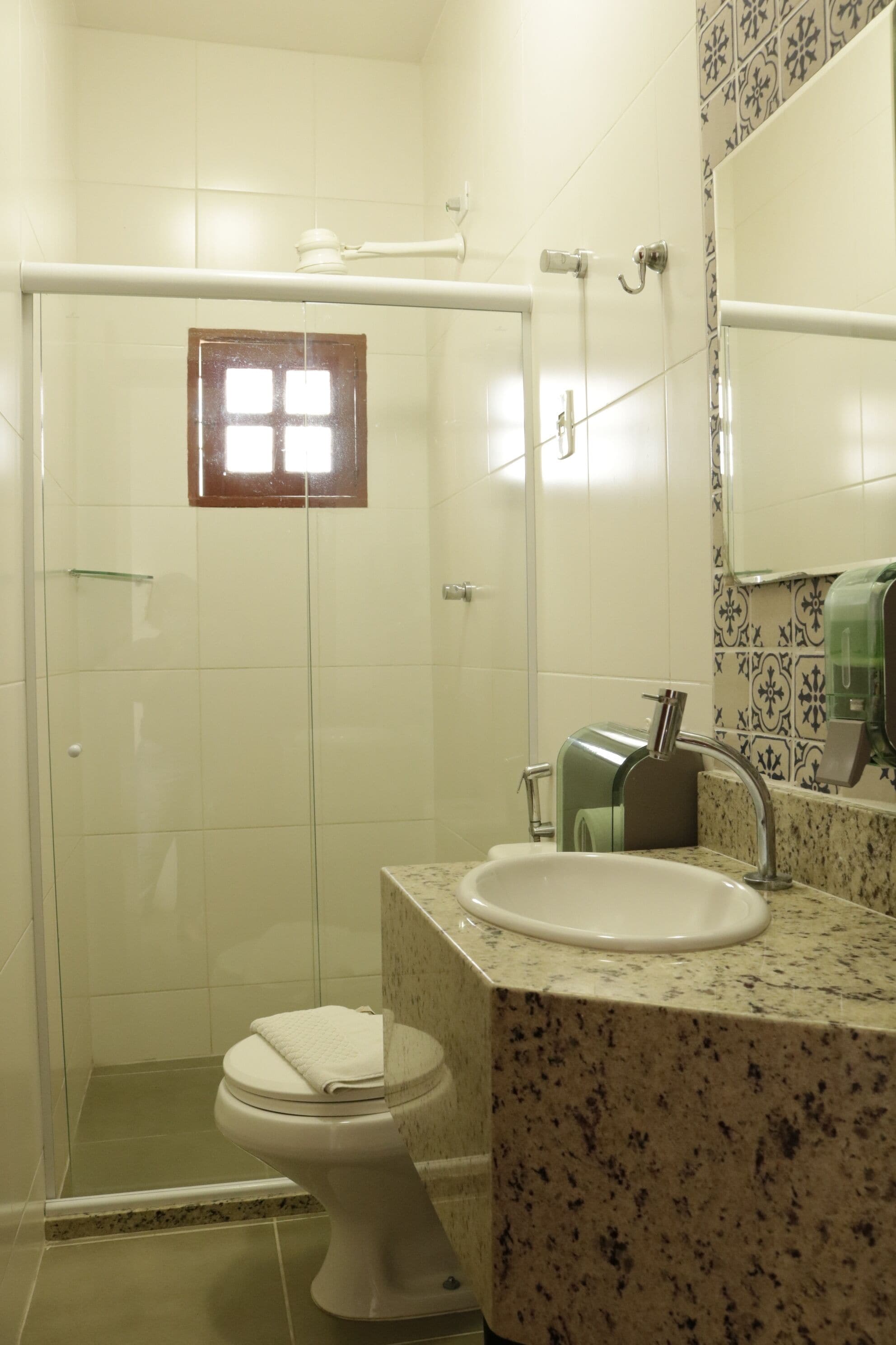 A bathroom with a glass-enclosed shower, a white toilet, and a marble sink with a soap dispenser.