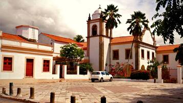 Un edificio blanco con puerta roja y un campanario, rodeado de palmeras y un patio empedrado.