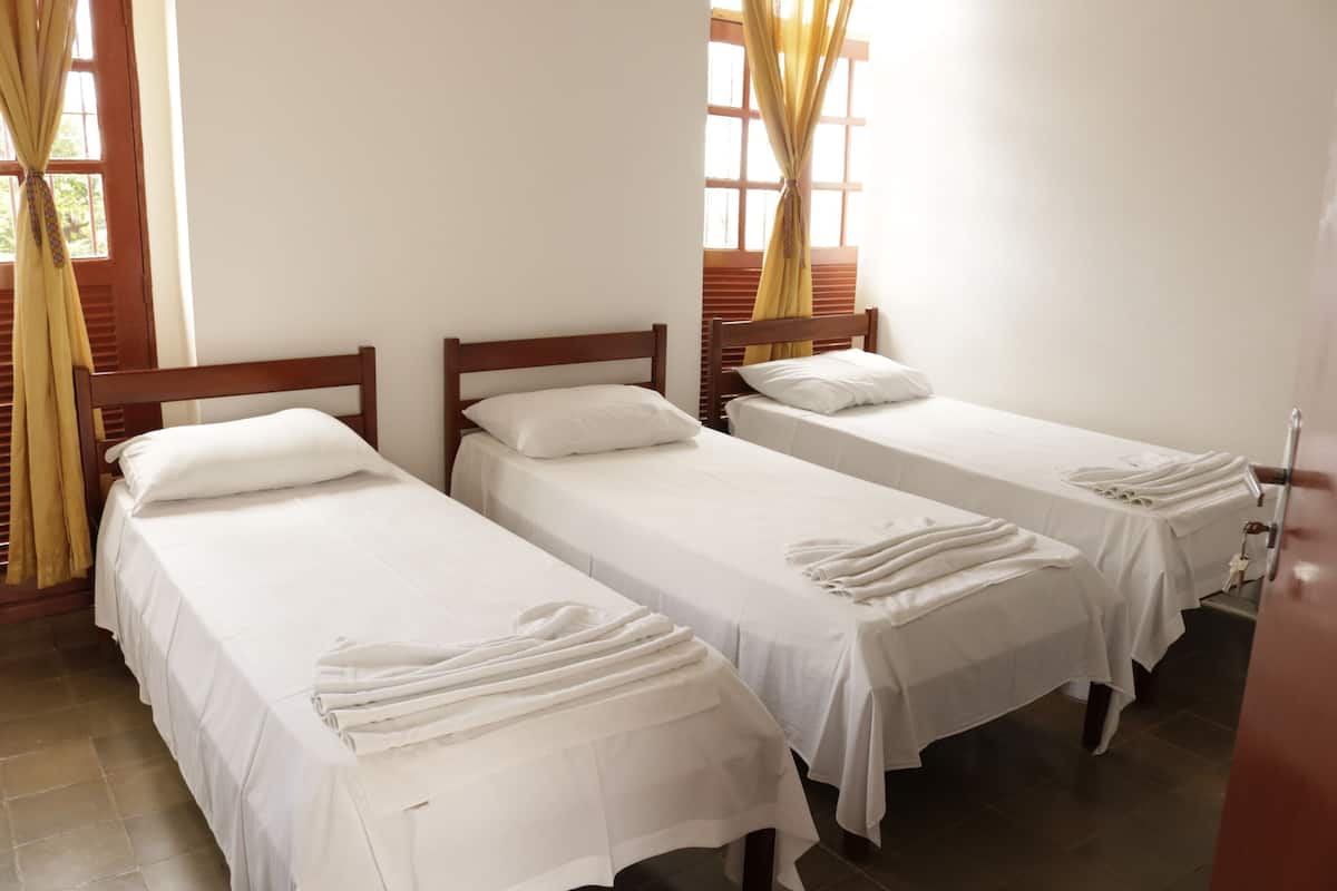 A hotel room with three single beds, each with white bedding and towels.