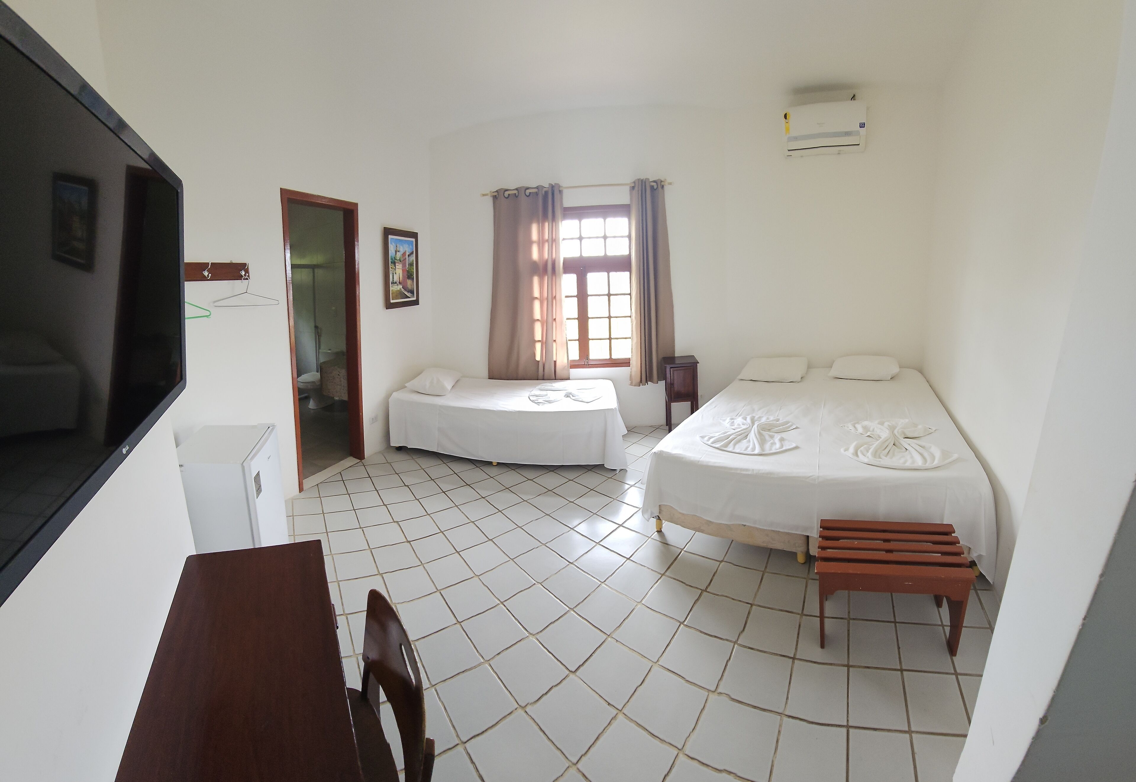 A hotel room with two beds, a desk, a chair, a TV, and a window with curtains.