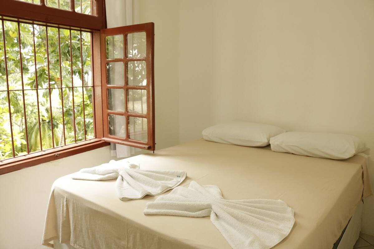 A room with a bed, white towels, and a window with a view of greenery.
