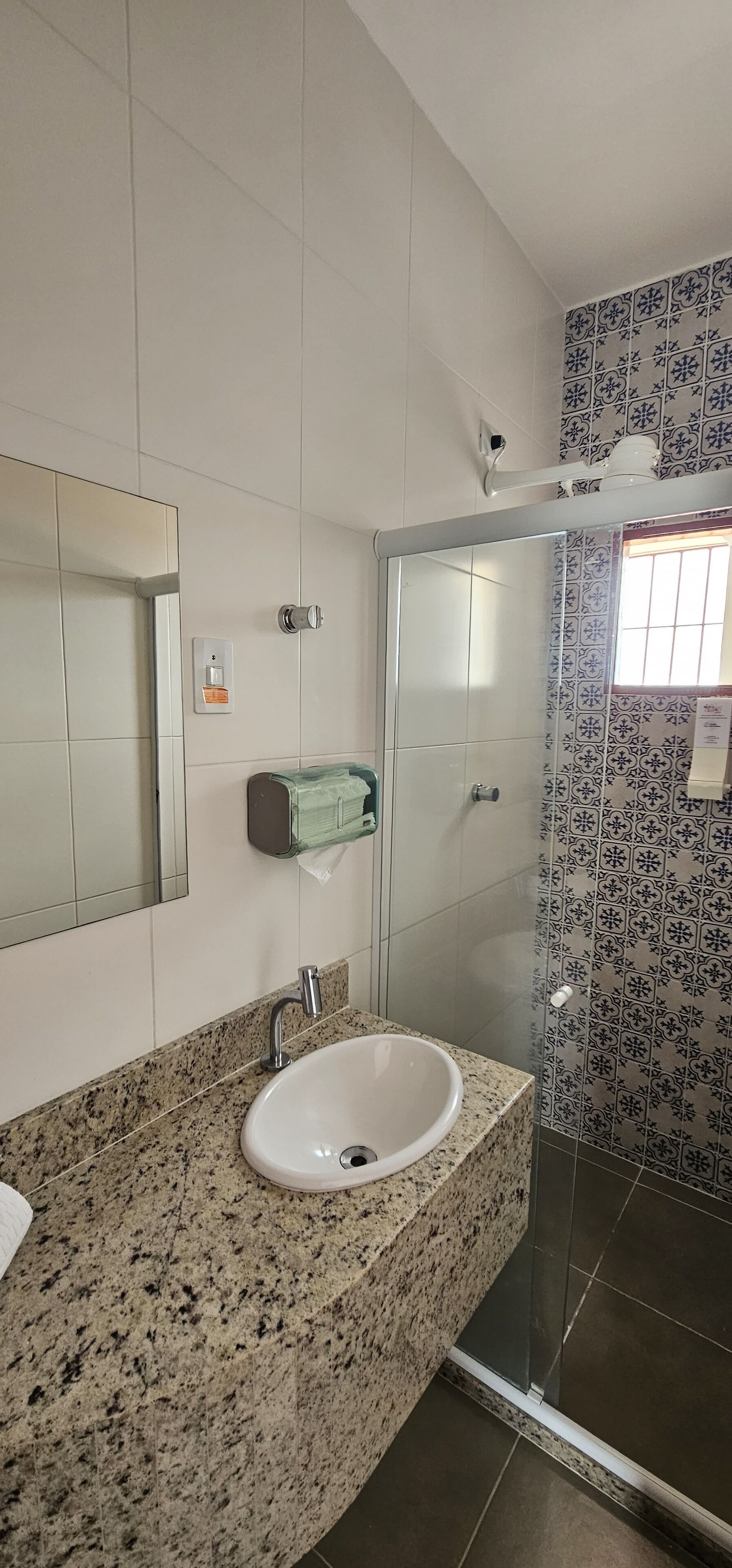 Un baño con encimera de granito, un lavabo blanco, un espejo, dispensador de toallas y una ducha con puerta de cristal.