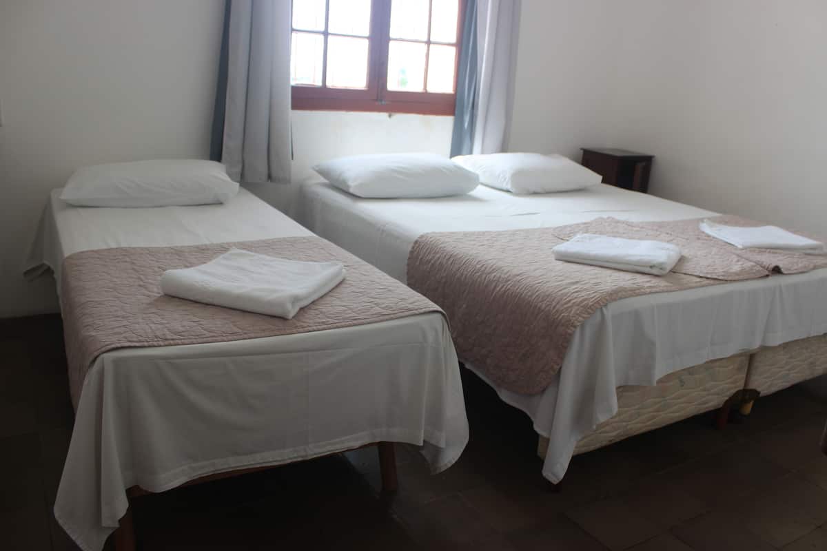 A room with two single beds, each with a white and pink quilt, and a small bedside table.