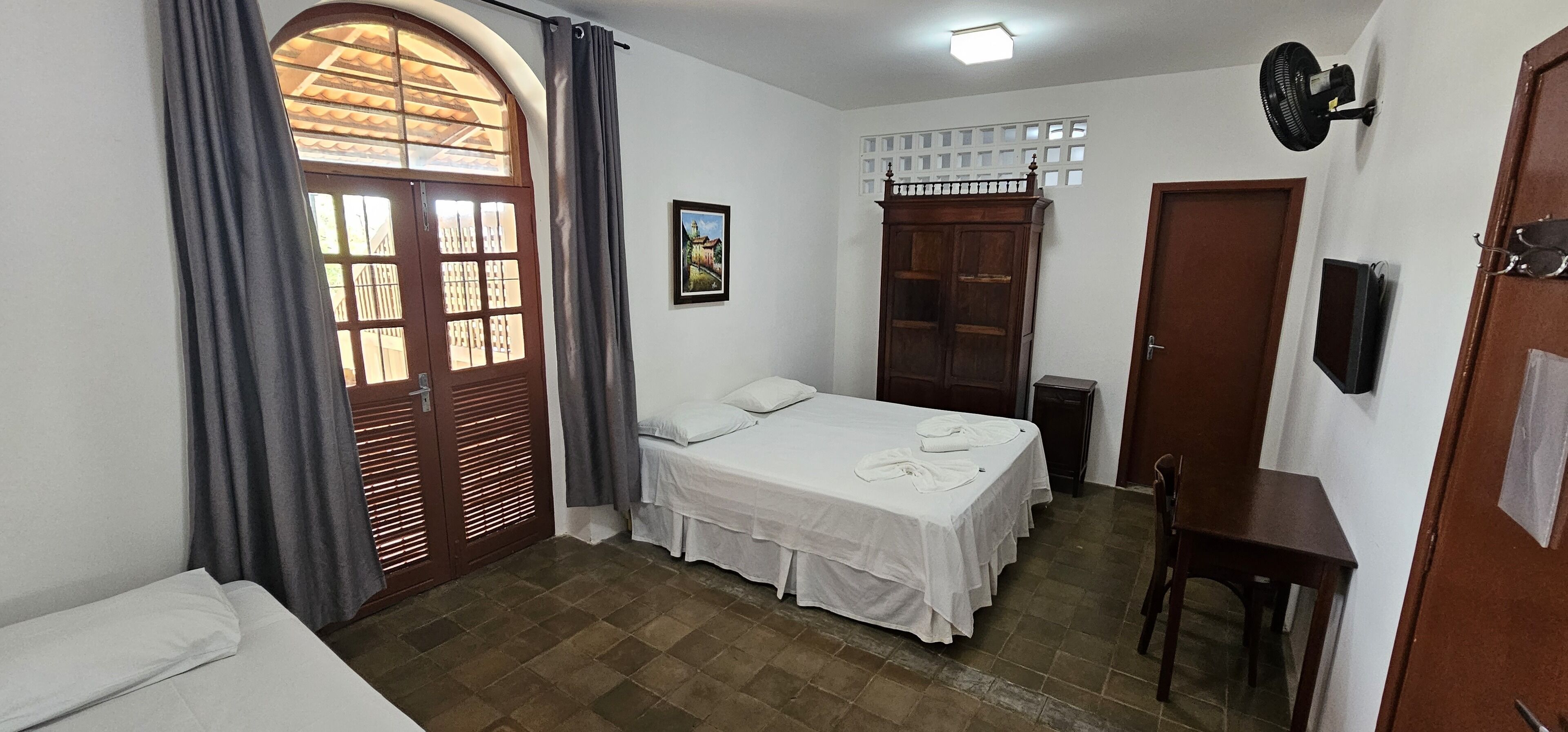 Una habitación pequeña y limpia con cama, escritorio, silla, armario y ventana con cortinas.