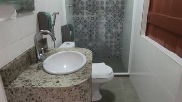 A bathroom with a granite countertop sink, a toilet, and a shower area.