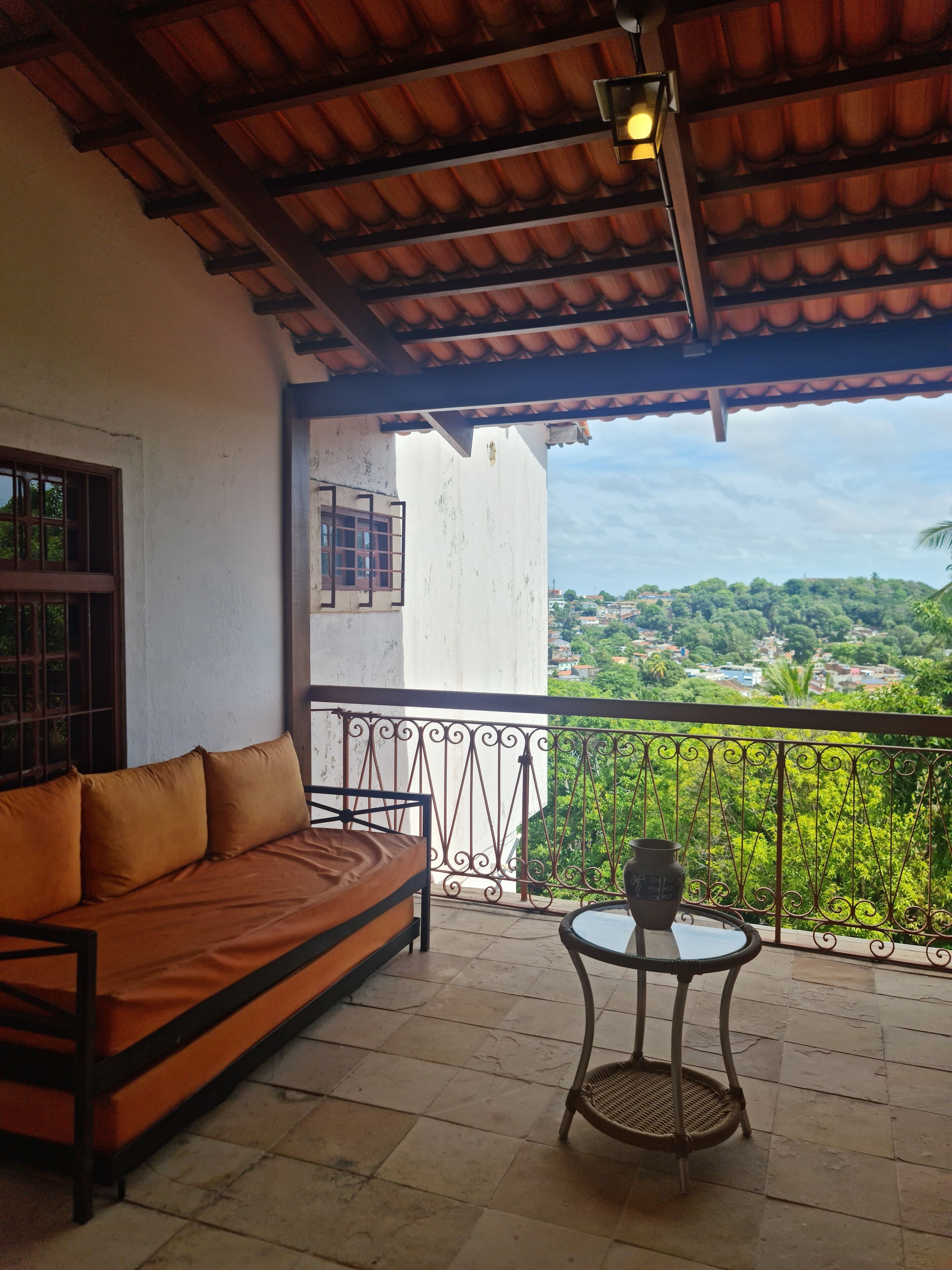 A balcony with a sofa and a table, overlooking a green landscape.