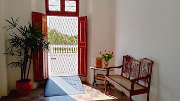 Una habitación con puerta roja, una planta en maceta, un banco y una pequeña mesa con un jarrón de flores.