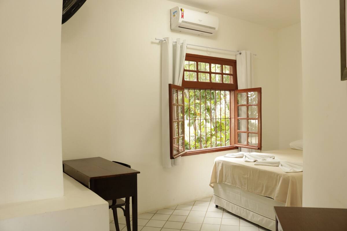A small, clean room with a bed, a desk, and a window with curtains.