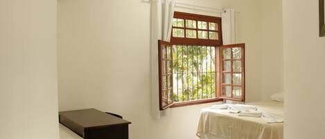 A small, clean room with a bed, a desk, and a window with curtains.