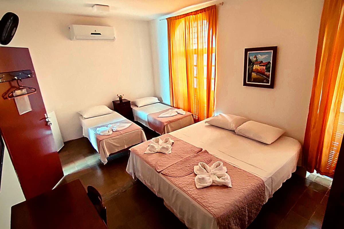 A hotel room with two beds, a desk, a chair, a wardrobe, and a painting on the wall.