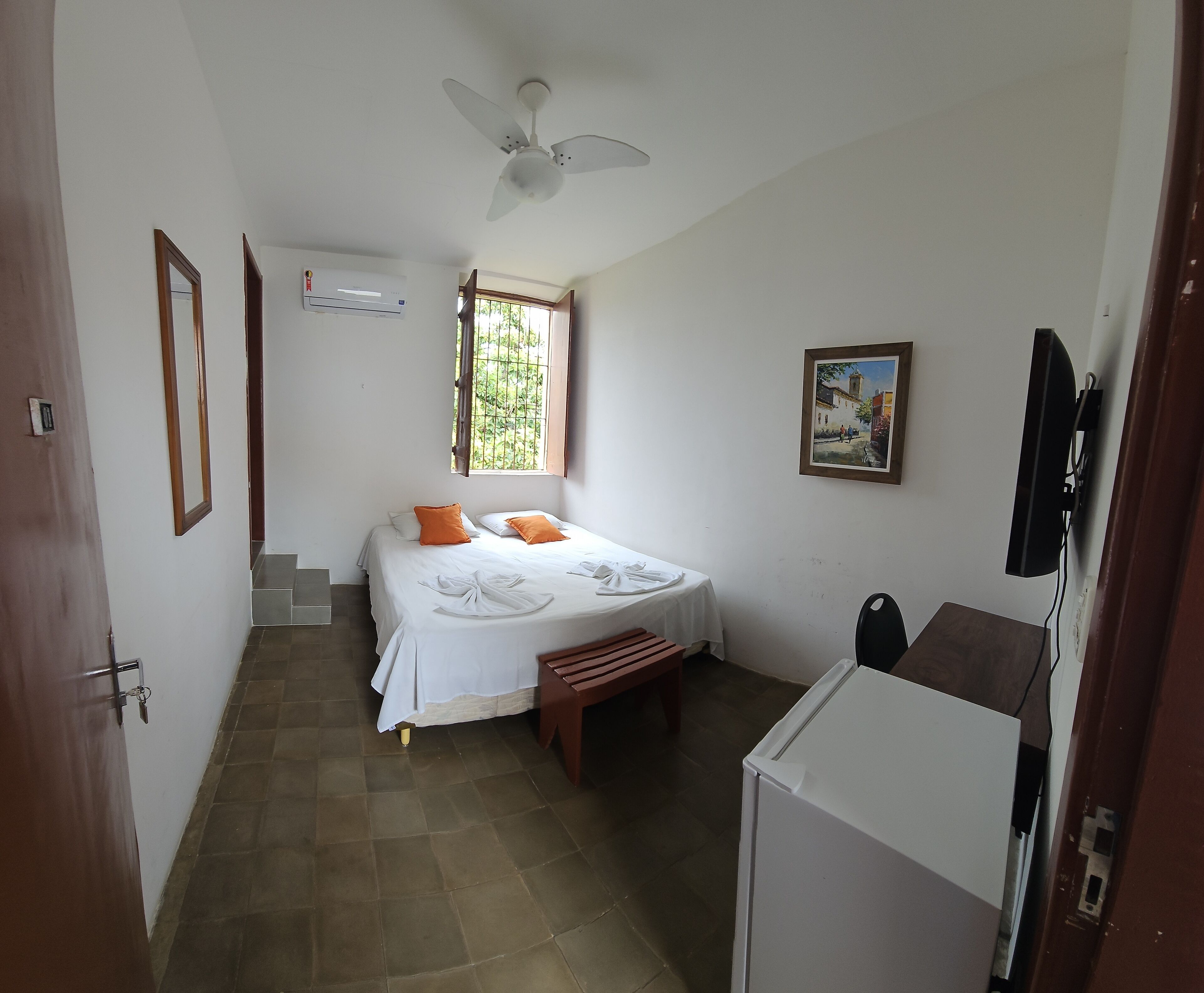 Un dormitorio con una cama, ventilador de techo, ventana, un cuadro y televisor.
