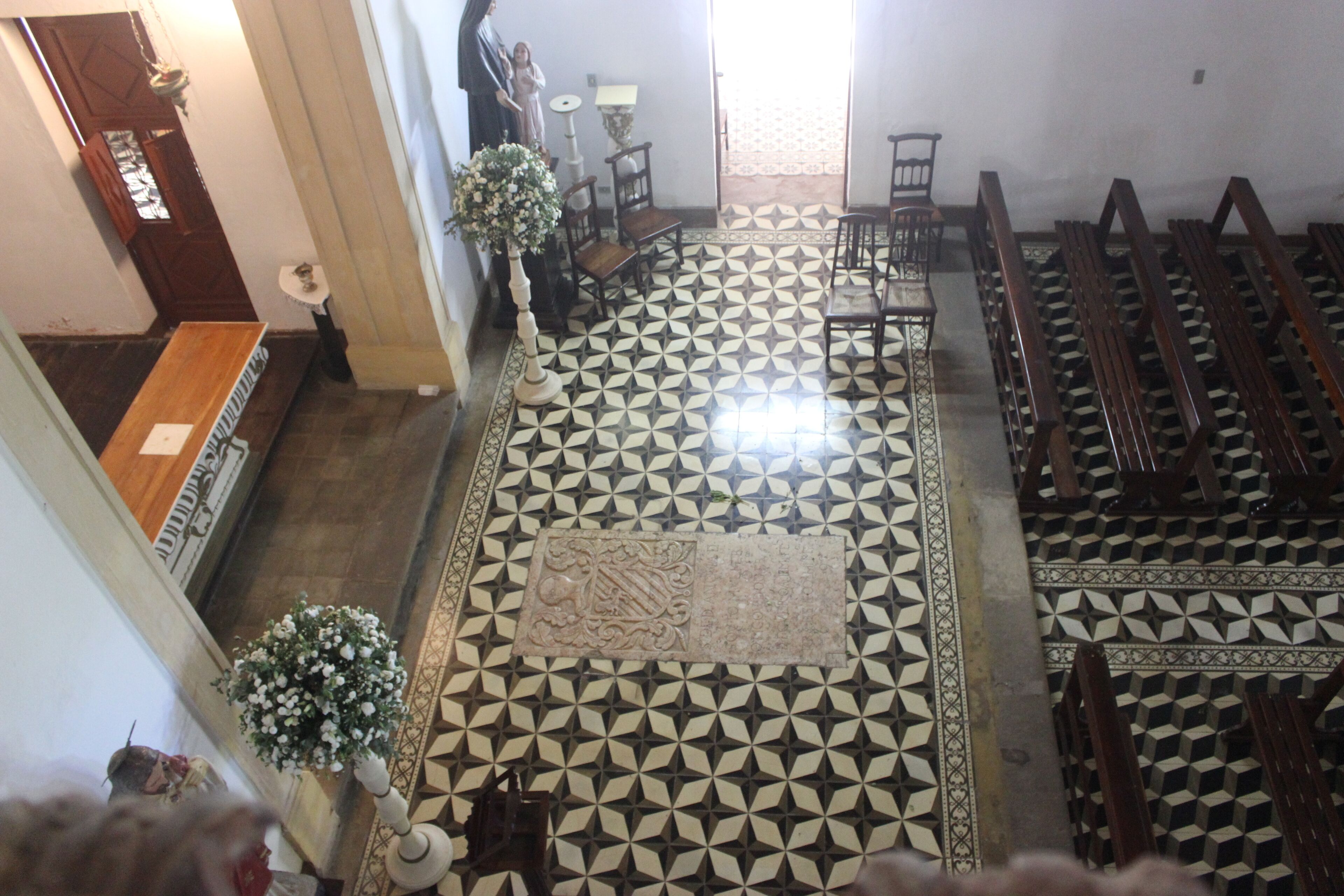 A church interior with a geometric patterned floor, wooden pews, a central aisle, and a statue.