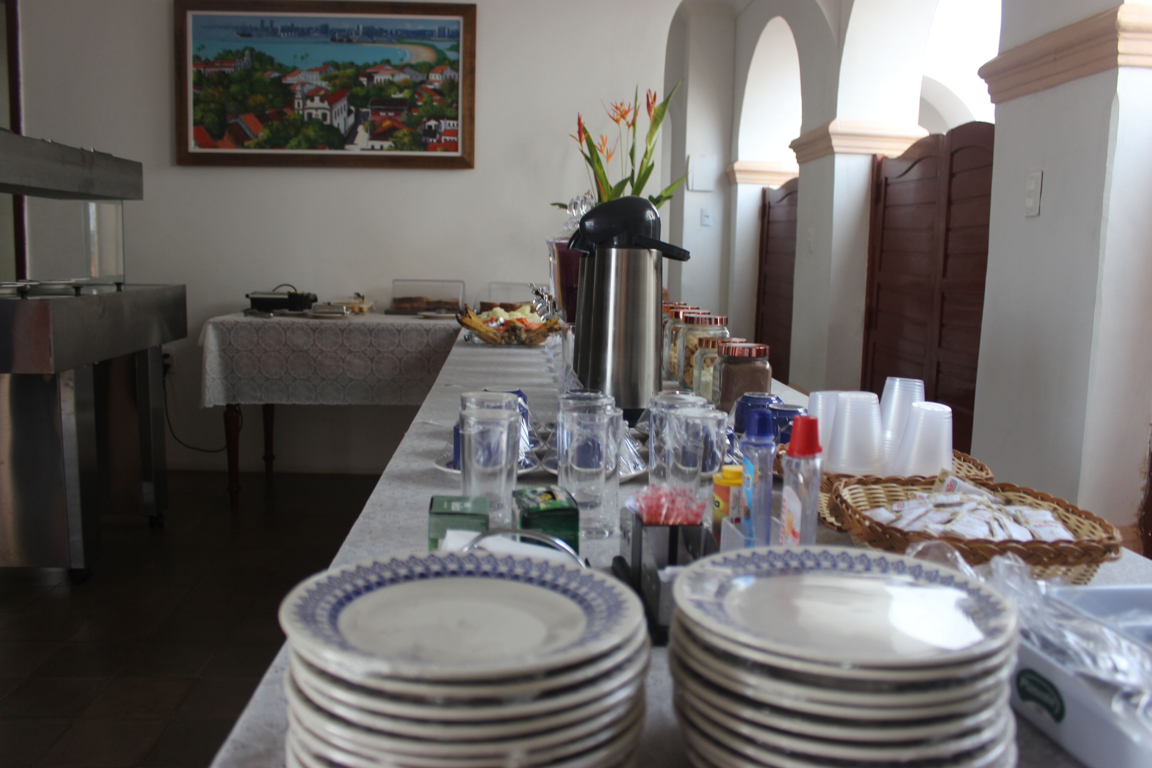 Un comedor con una larga mesa dispuesta para una comida, un cuadro en la pared y una zona de cocina al fondo.