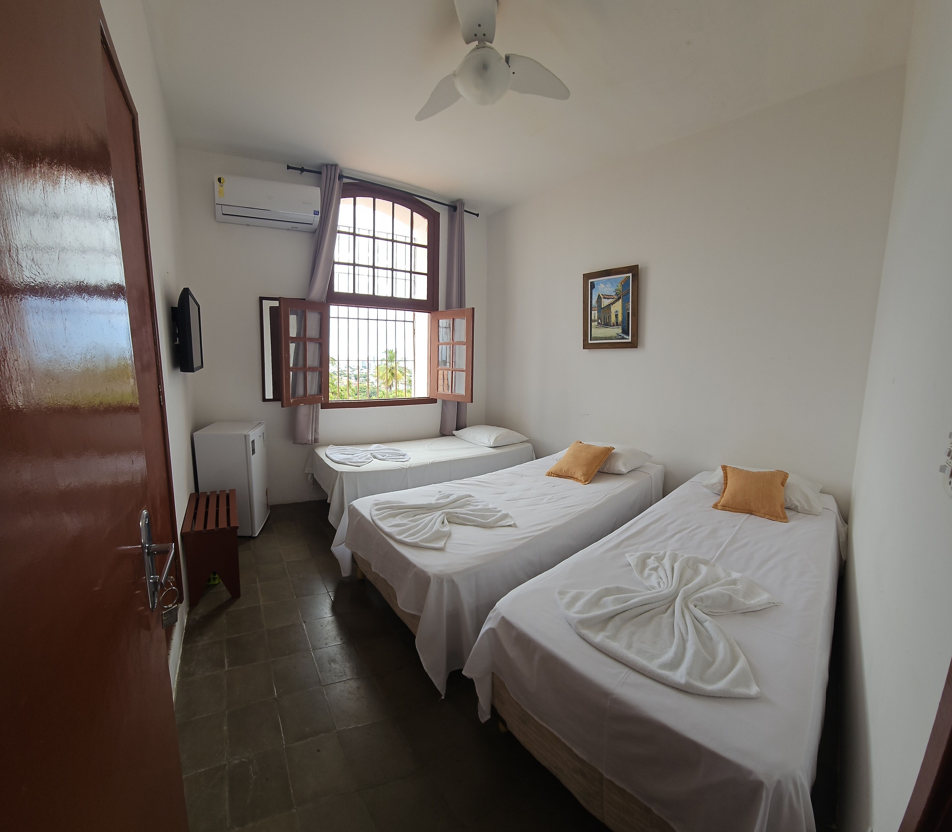 A room with two beds, a window with curtains, a ceiling fan, and a wall-mounted air conditioner.