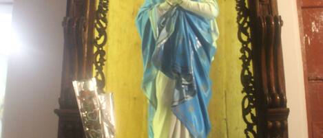 Een standbeeld van een religieuze figuur met een halo, omringd door versierde houtsnijwerken en een vaas met bloemen.