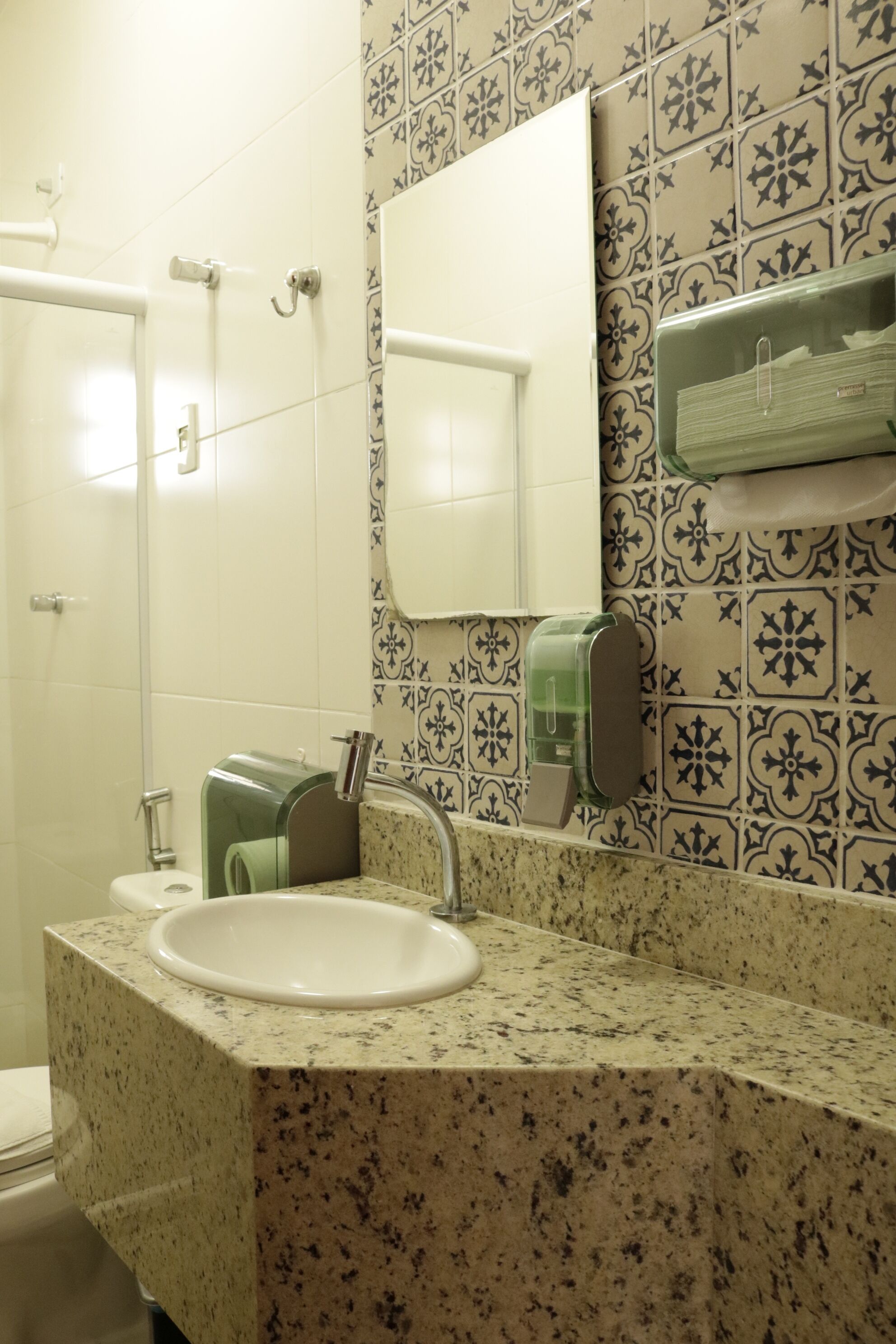 Un baño con lavamanos, espejo, dispensador de toallas y retrete.