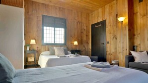 A wooden-paneled room with two beds, a sofa, and a lamp.