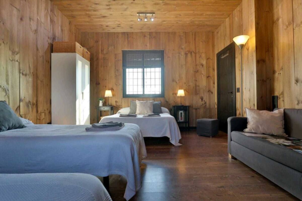 A wooden cabin room with two beds, a sofa, and a window.