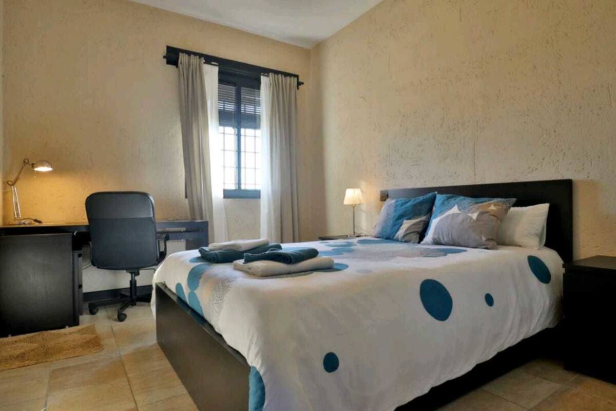 A hotel room with a bed, desk, chair, and a window with curtains.