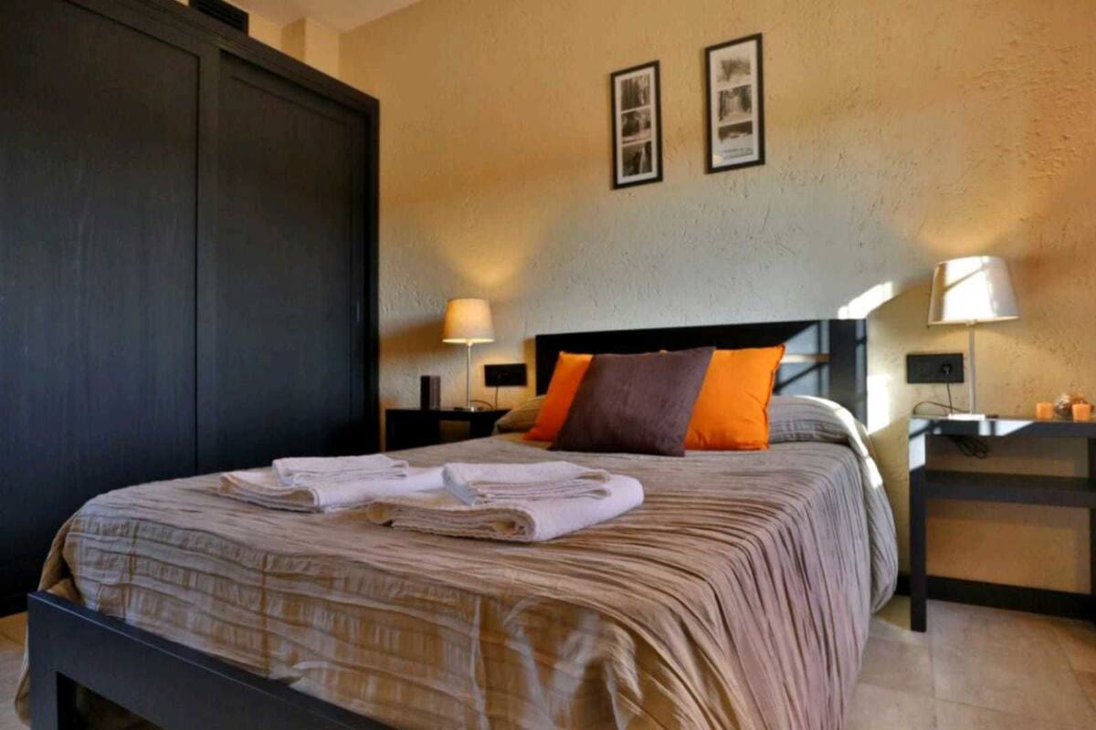 A neatly made bed with a striped bedspread and two pillows, a nightstand with a lamp, and two framed pictures on the wall.