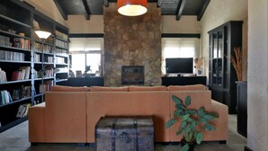 A cozy living room with a stone fireplace, a large sectional sofa, a bookshelf, and a television.