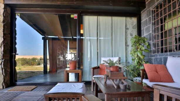 An open-air patio with wooden furniture, a white sofa, and potted plants.