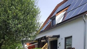 Una casa con paneles solares en el techo, una escalera de madera y un camino de entrada pavimentado.
