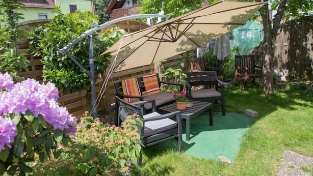 Un patio al aire libre con una mesa y sillas, rodeado de follaje y una cerca de madera.