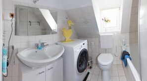 A modern bathroom with a sink, washing machine, toilet, and a mirror. - Apartment Welcome (Allersberg)